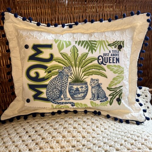 white textured pillow with navy pom trim and interchangeable mom snap graphic reading a title just above queen